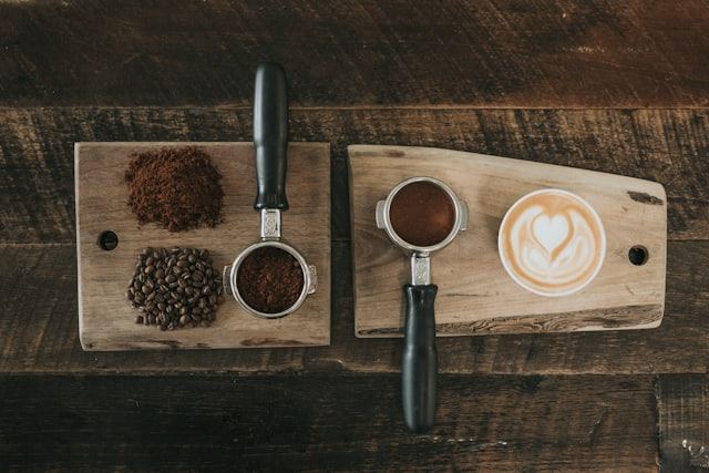 Two portafilters with ground coffee and a latte on a wooden board